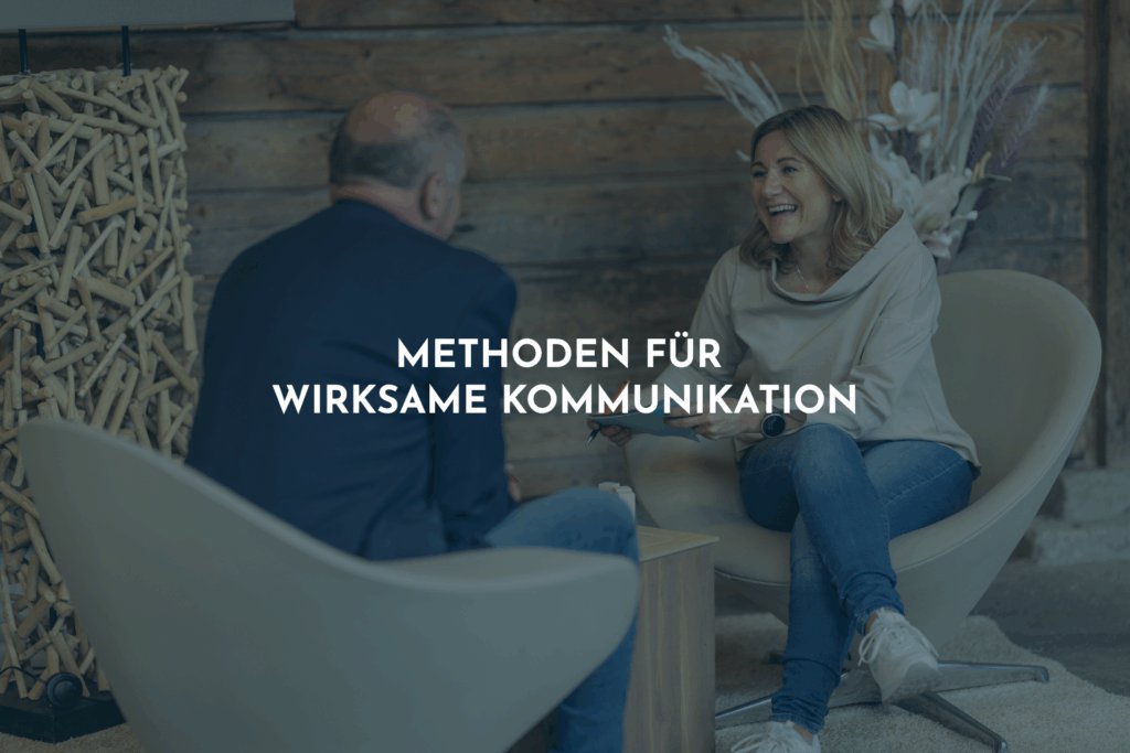 Ein Mann und eine Frau sitzen sich gegenüber, der Mann sitzt mit dem Rücken zur Kamera. Die Frau lächelt und hält einen Kugelschreiber und Kärtchen in den Händen.