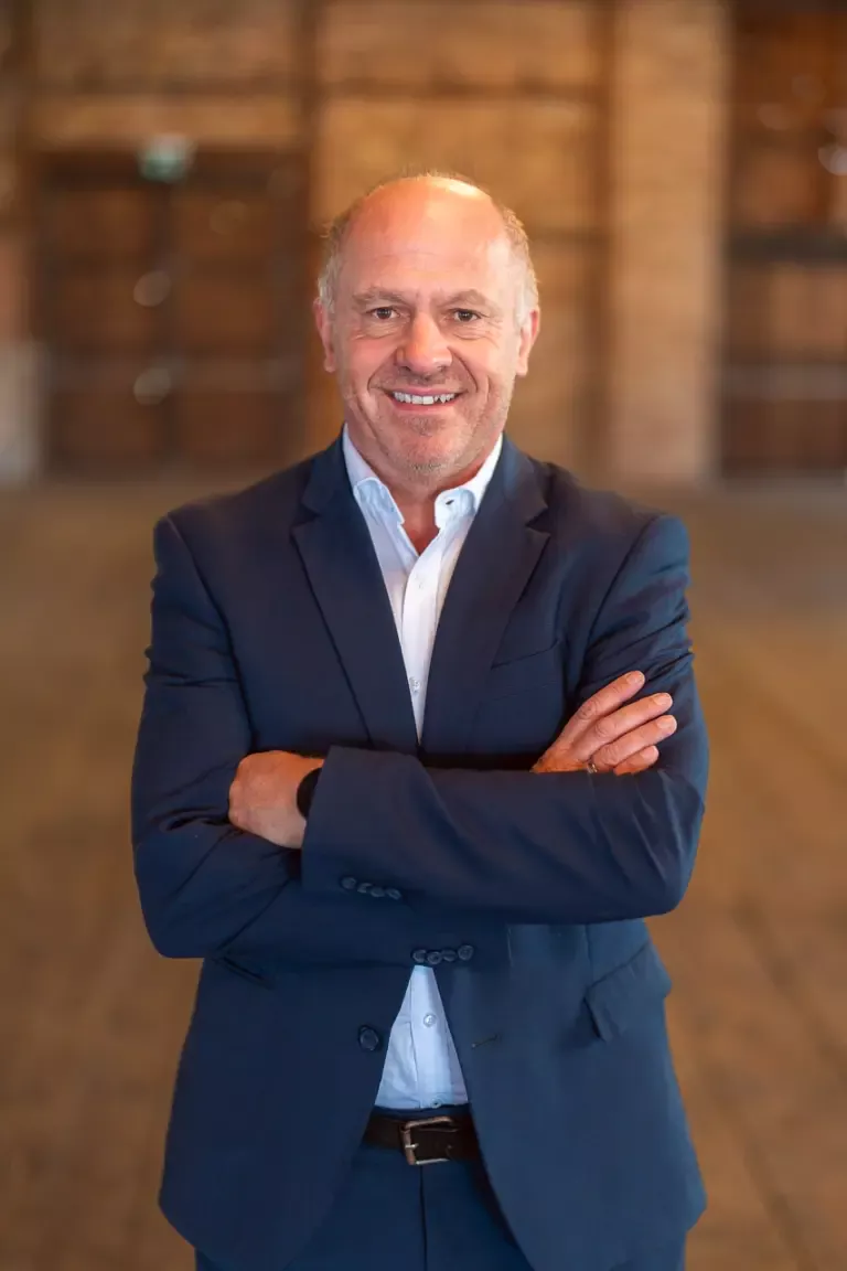 Walter Aigner_Ein Mann in Anzug steht in einem leeren Raum und lächelt freundlich in die Kamera
