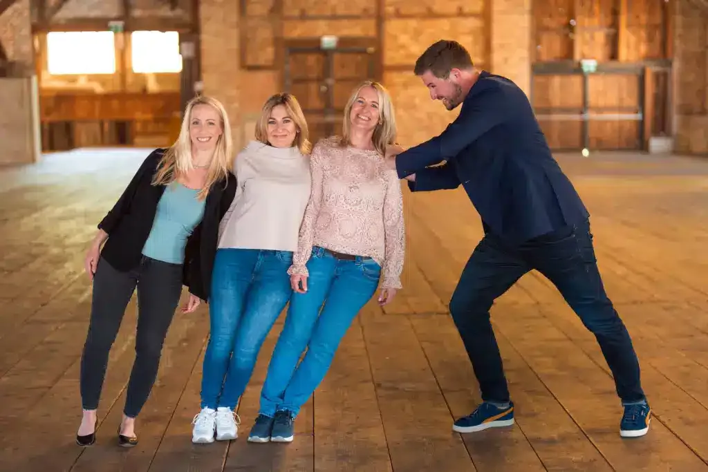 Drei Frauen lehnen sich auf die Seite, ein Mann stemmt sich dagegen.