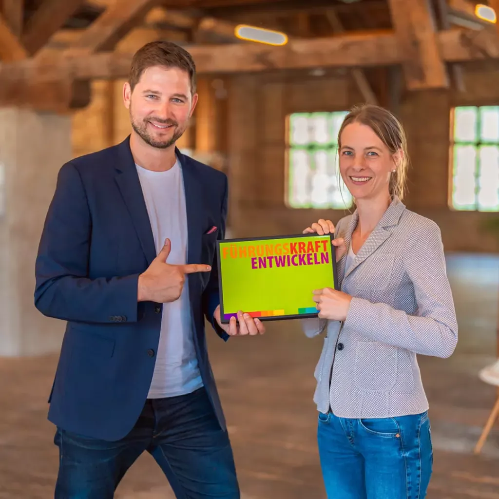 Ein Mann und eine Frau halten gemeinsam eine Karte mit der Beschriftung "Führungskraft entwickeln".