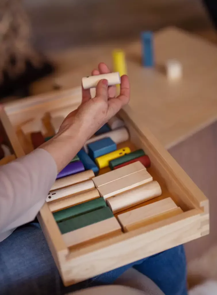 Systembrett. Eine Hand greift nach Holzbausteinen in einer Holzbox.