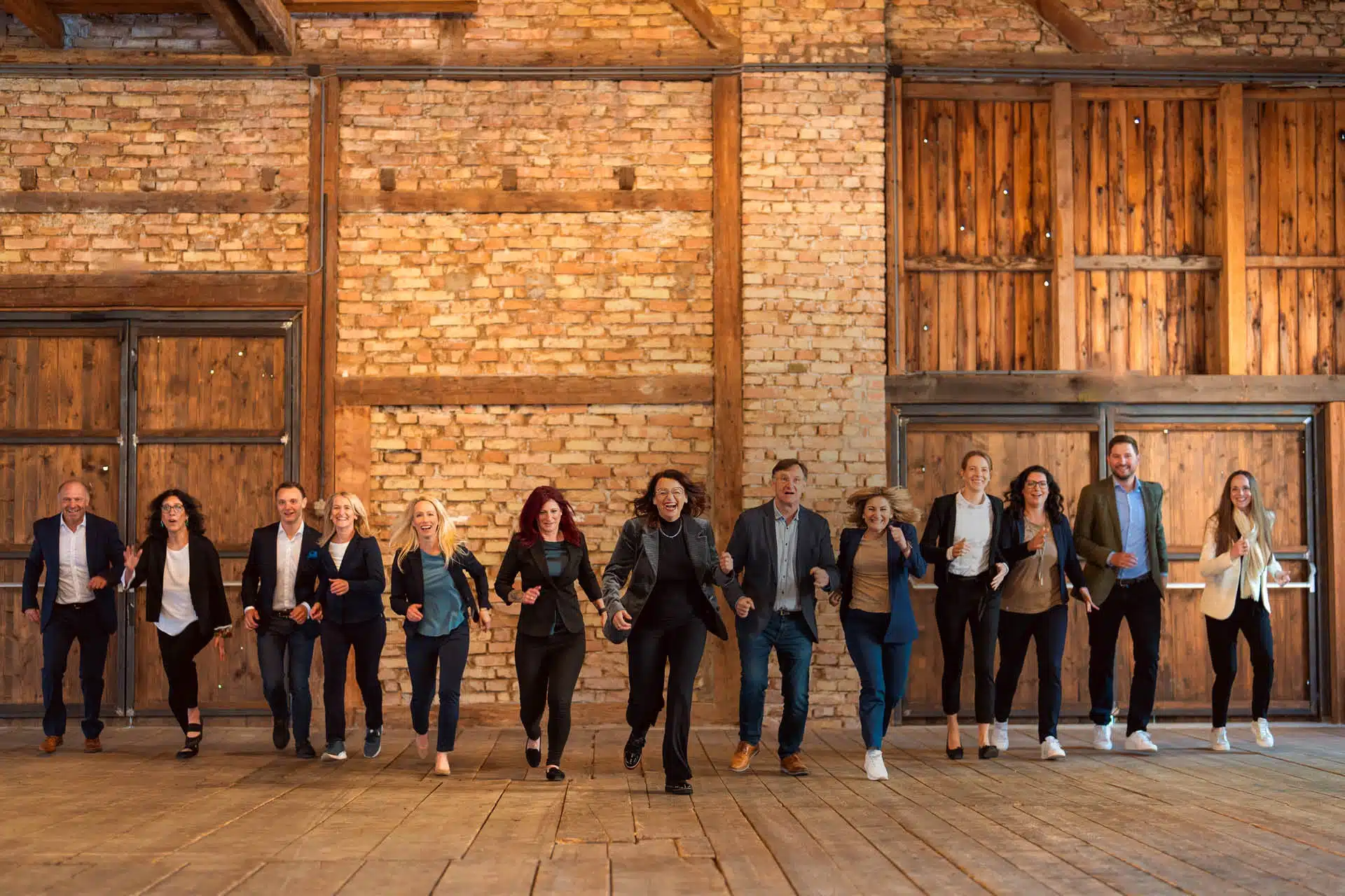 Teamfoto mit dreizehn Personen die lachen undd auf die Kamera zulaufen