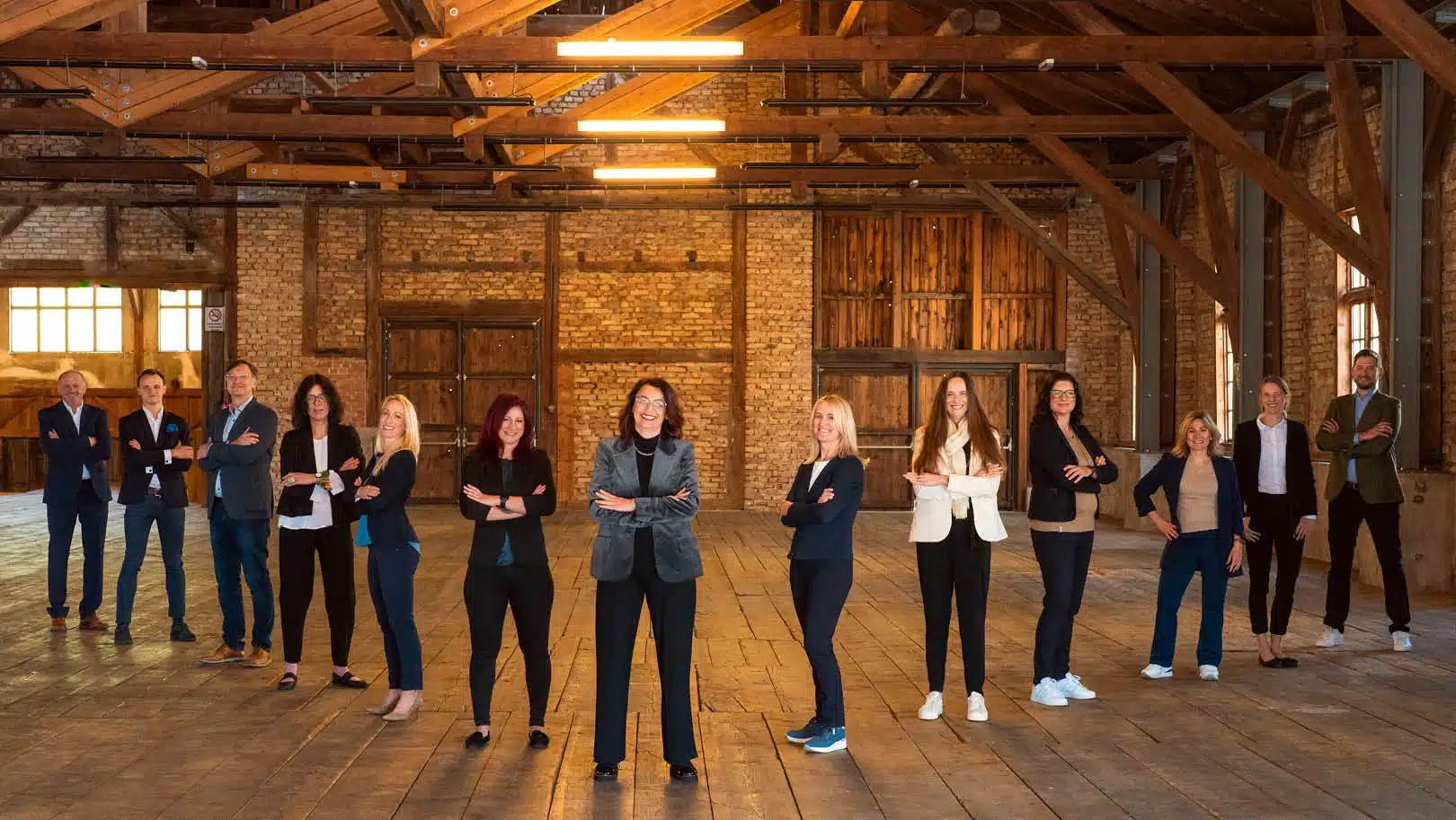 Frauen und Männer im Business Outfit stehen mit verschränkten Armen in Pfeilformation in einer Scheune.