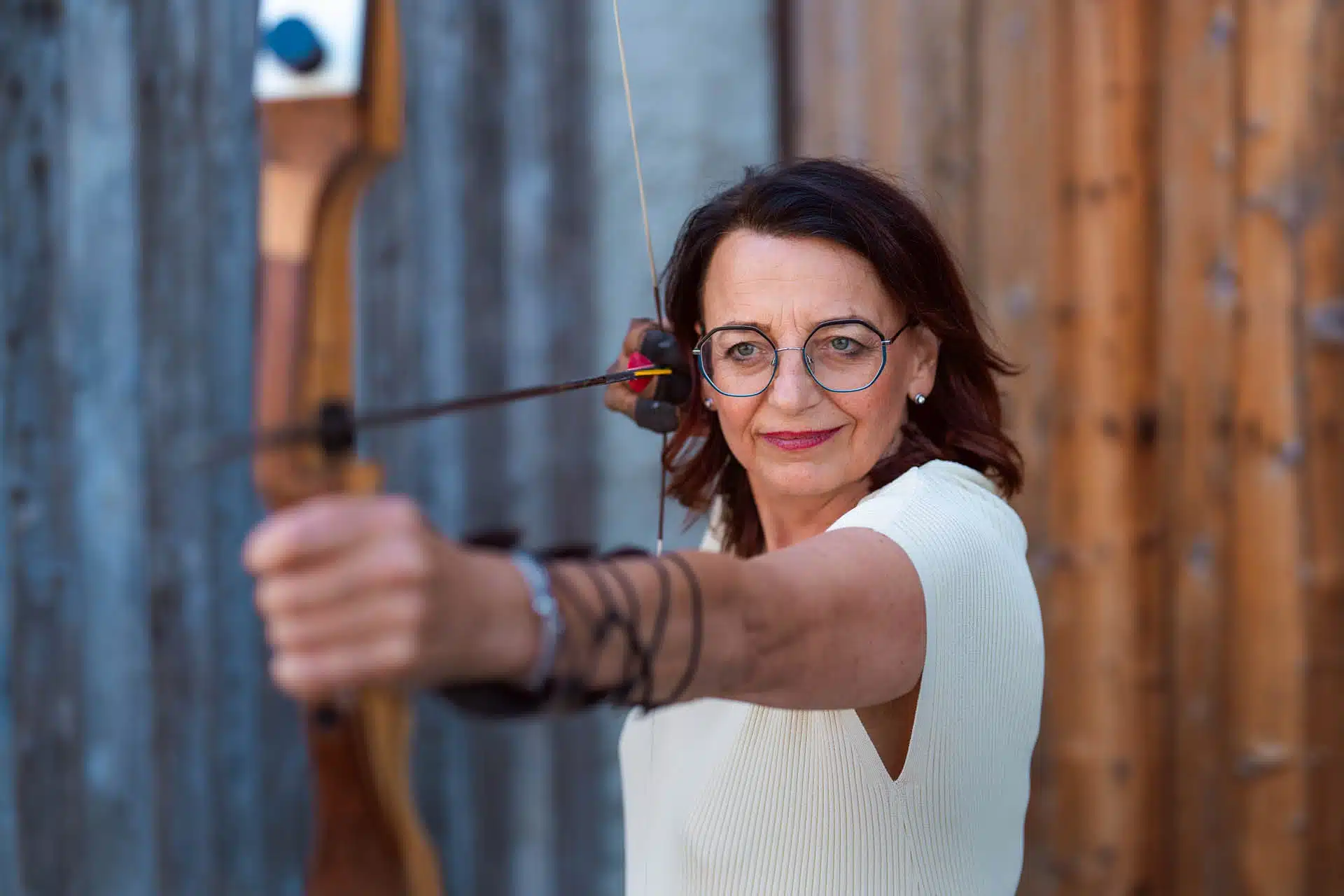 Eine Frau mit fokussiertem Blick hält Pfeil und Bogen in den Händen, bereit zum Schuss.