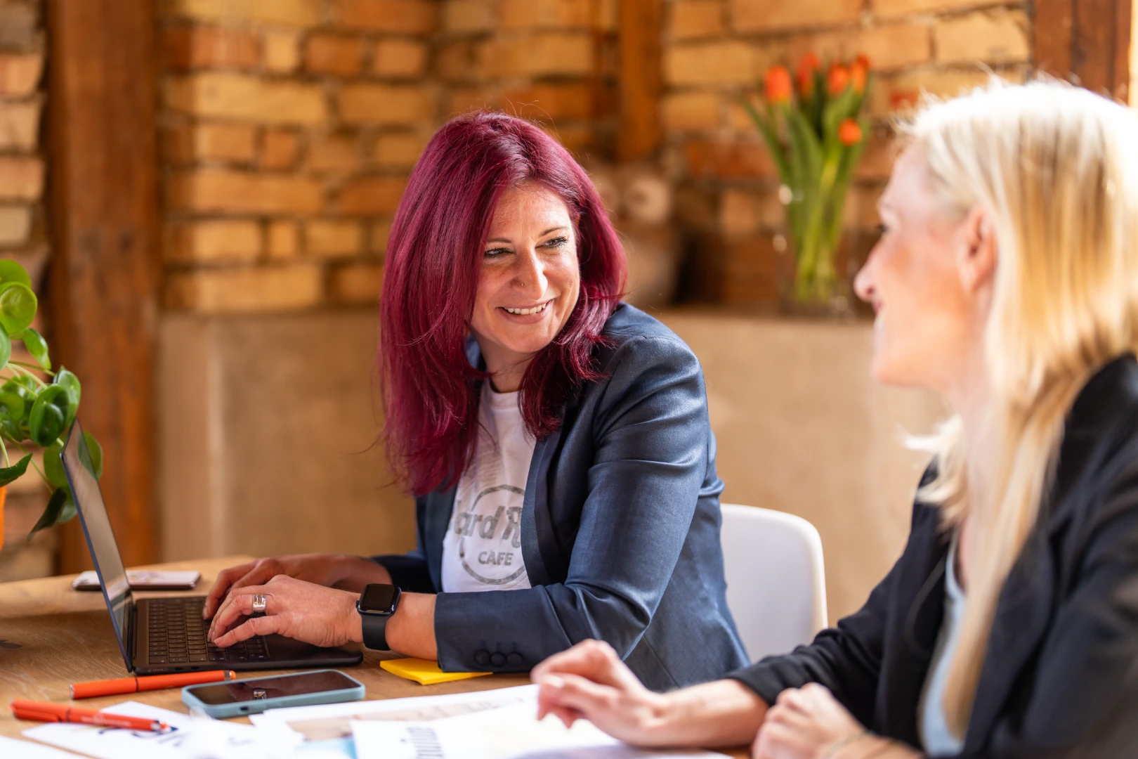 Zwei Frauen im Business Outfit sitzen an einem Besprechungstisch und unterhalten sich.