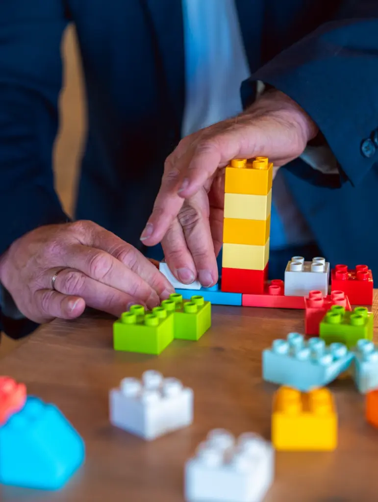 Bunte Legobausteine liegen auf einem Tisch. Man sieht zwei Hände, sie etwas daraus bauen.