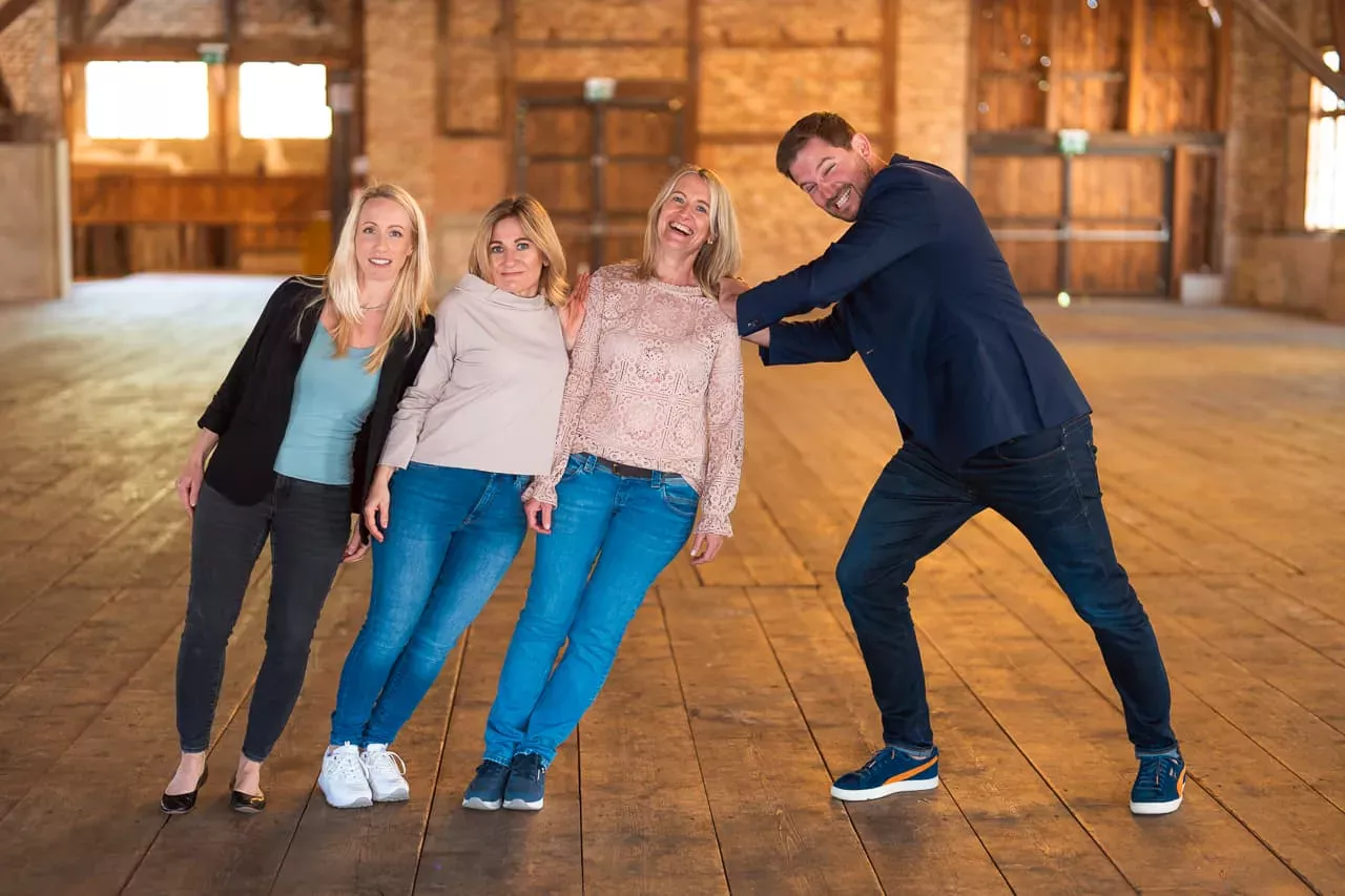 Drei Personen die sich zusammen gegen eine Person lehnen und diese hält mit angestrengtem Gesicht dagegen
