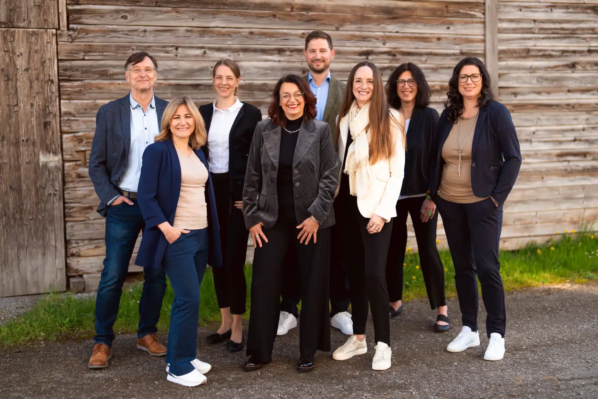 Teamfoto mit acht Personen im Außenbereich vor Holzhintergrund